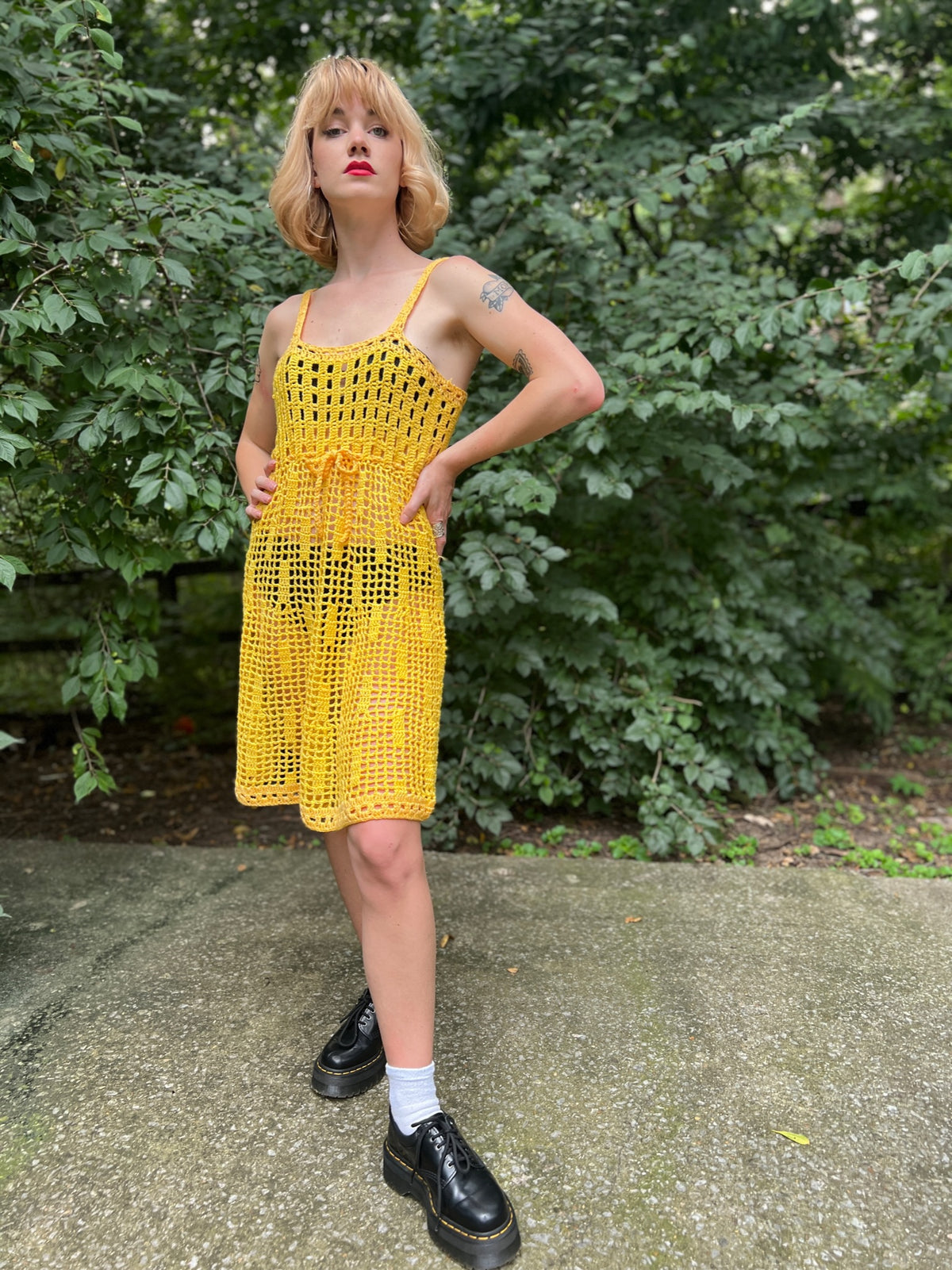 Yellow crocheted dress with thin straps, a drawstring tie at the empire waist and a flared skirt, worn by a model