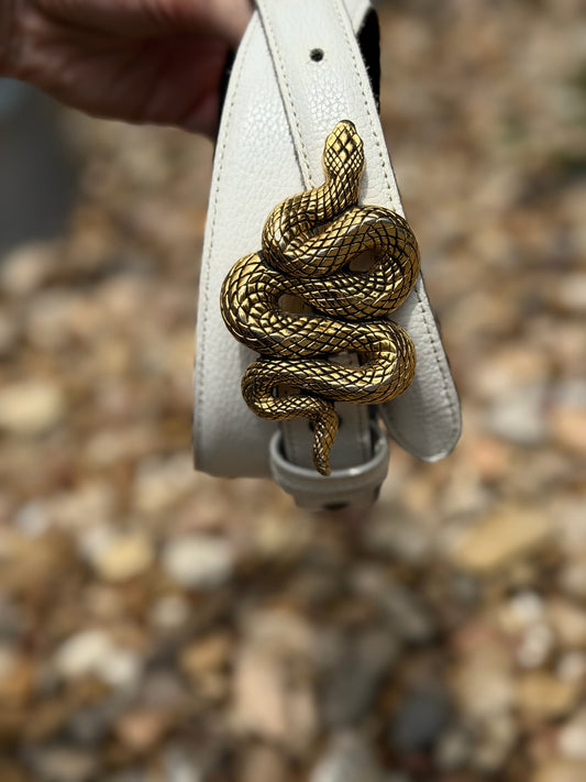 Close-up of the coiled snake buckle on the white leather belt, held in a hand
