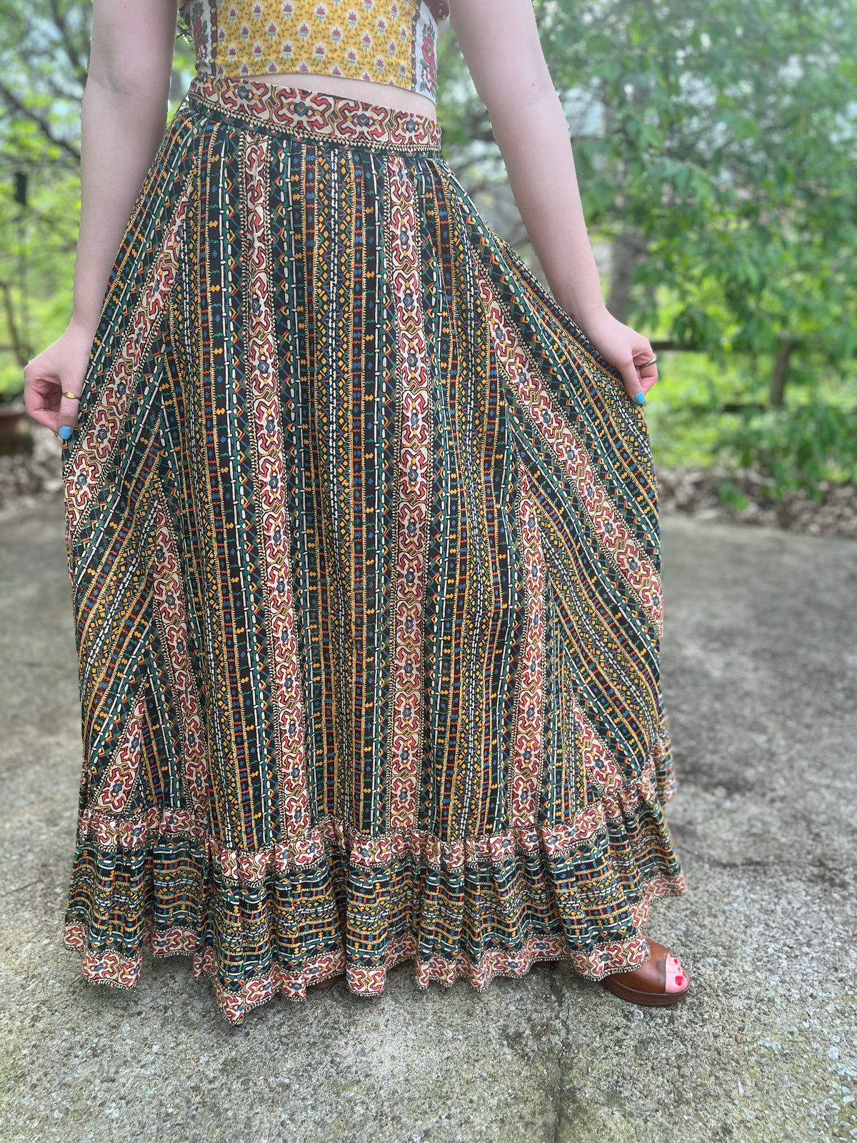 Full maxi skirt with a southwestern print in gold, black, green, red, blue and tan and a ruffled hem, held out by a model