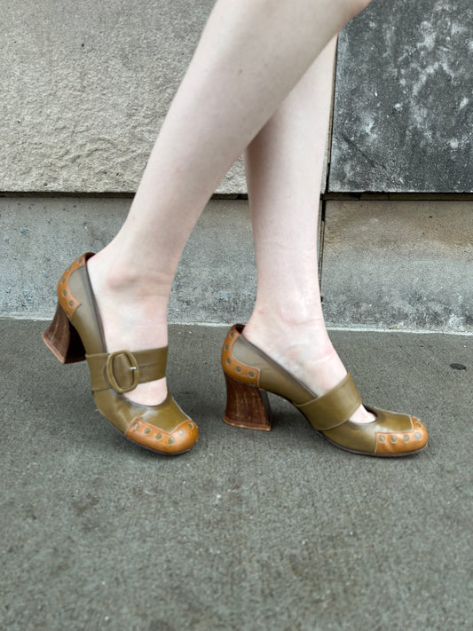 Both shoes on the model from the side, showing the wide buckle strap, perforations and chunky heels