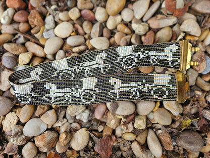 Beaded belt folded back on itself showing repeating white horse and carriage scenes on black and the brass closure ends