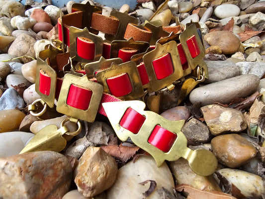 Red leather and brass belt with hanging brass pendants, coiled on pebbles