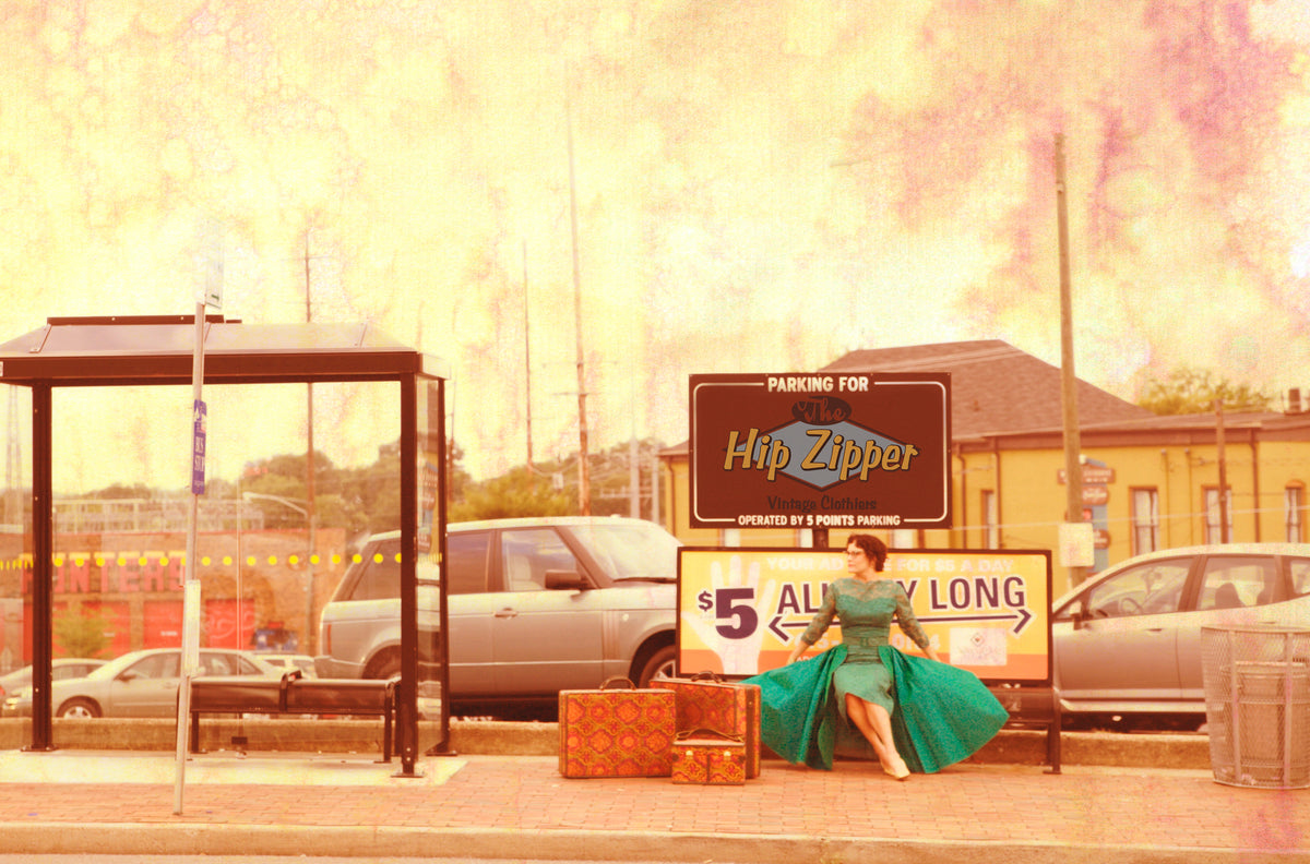 Person in a green dress seated beside suitcases, next to a Hip Zipper parking sign