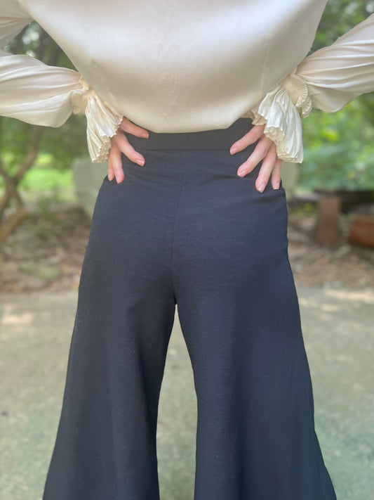 Back view of high-waisted black knit pants with a waistband and wide legs, worn by a model with a blouse
