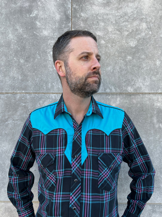 Black western snap shirt with pink and turquoise plaid, a turquoise yoke and two flap pockets, worn by a model