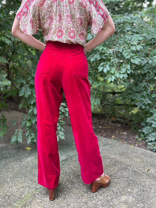Back view of cranberry red velour bell bottom pants with two back patch pockets and belt loops, worn by a model
