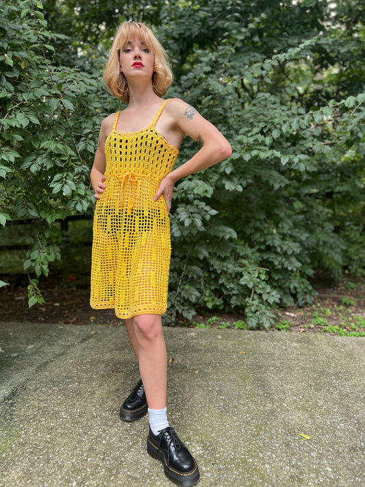Yellow crocheted dress with thin straps, a drawstring tie at the empire waist and a flared skirt, worn by a model