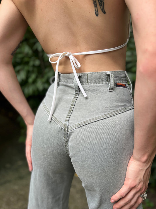Back view of slate green jeans with stitching at the hip and a label at the waistband, on a model