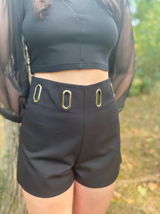 Black shorts with silver grommets around the waist, worn by a model with a cropped top