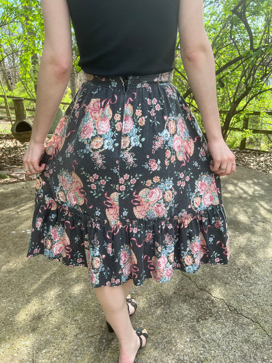 Back view of a black skirt with a pink floral basket print and gathered hem, worn by a model