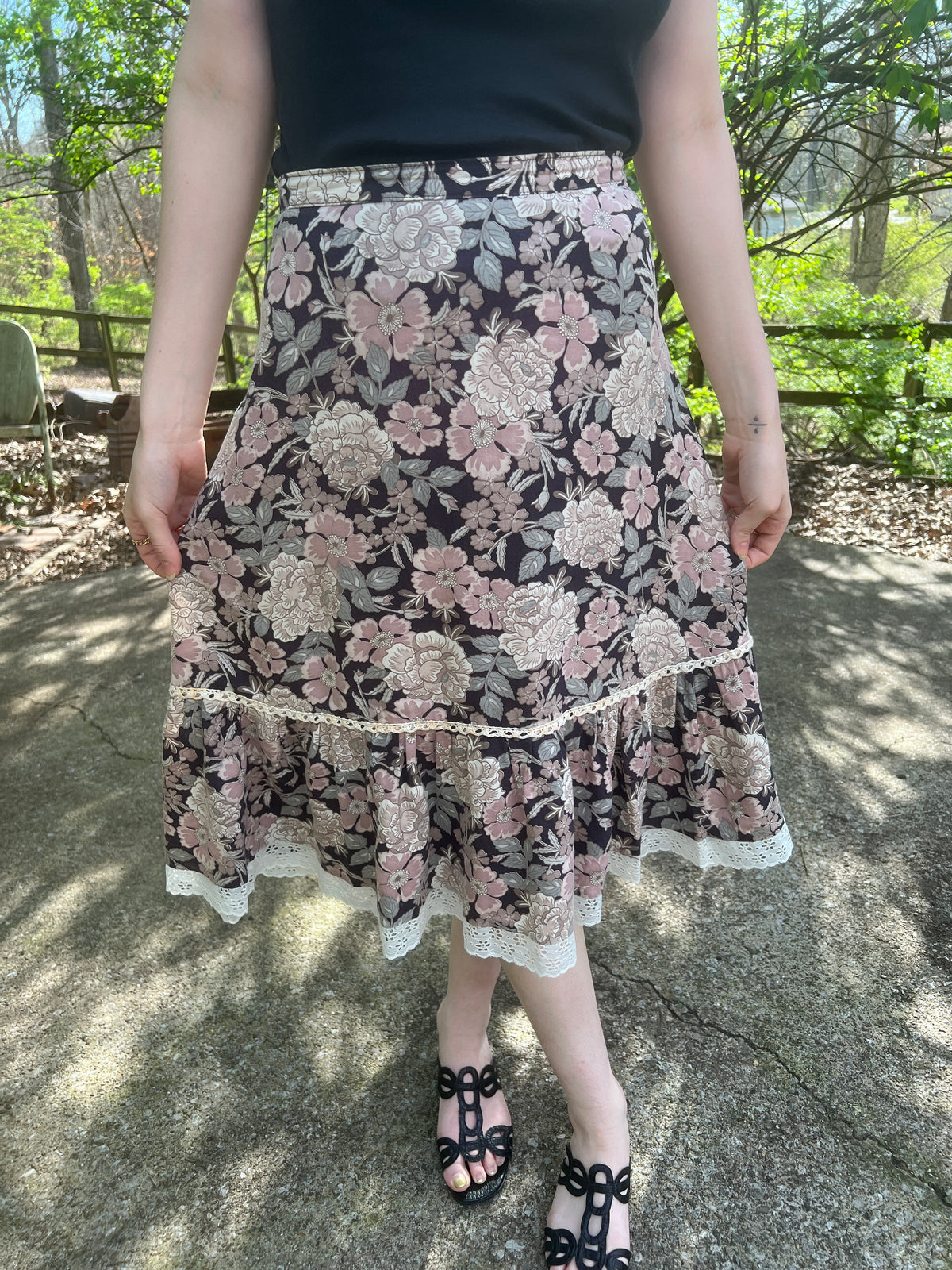 Black skirt with a pink and green floral print, crocheted detail and eyelet trim at the hem, worn by a model