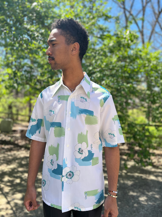 White short sleeve button-down shirt with a blue and green tropical floral print, worn by a model