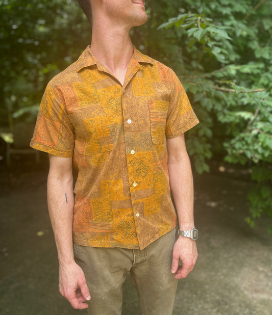 Short-sleeve cotton shirt with a gold, teal, orange and brown botanical print, collar and chest pockets, worn by a model