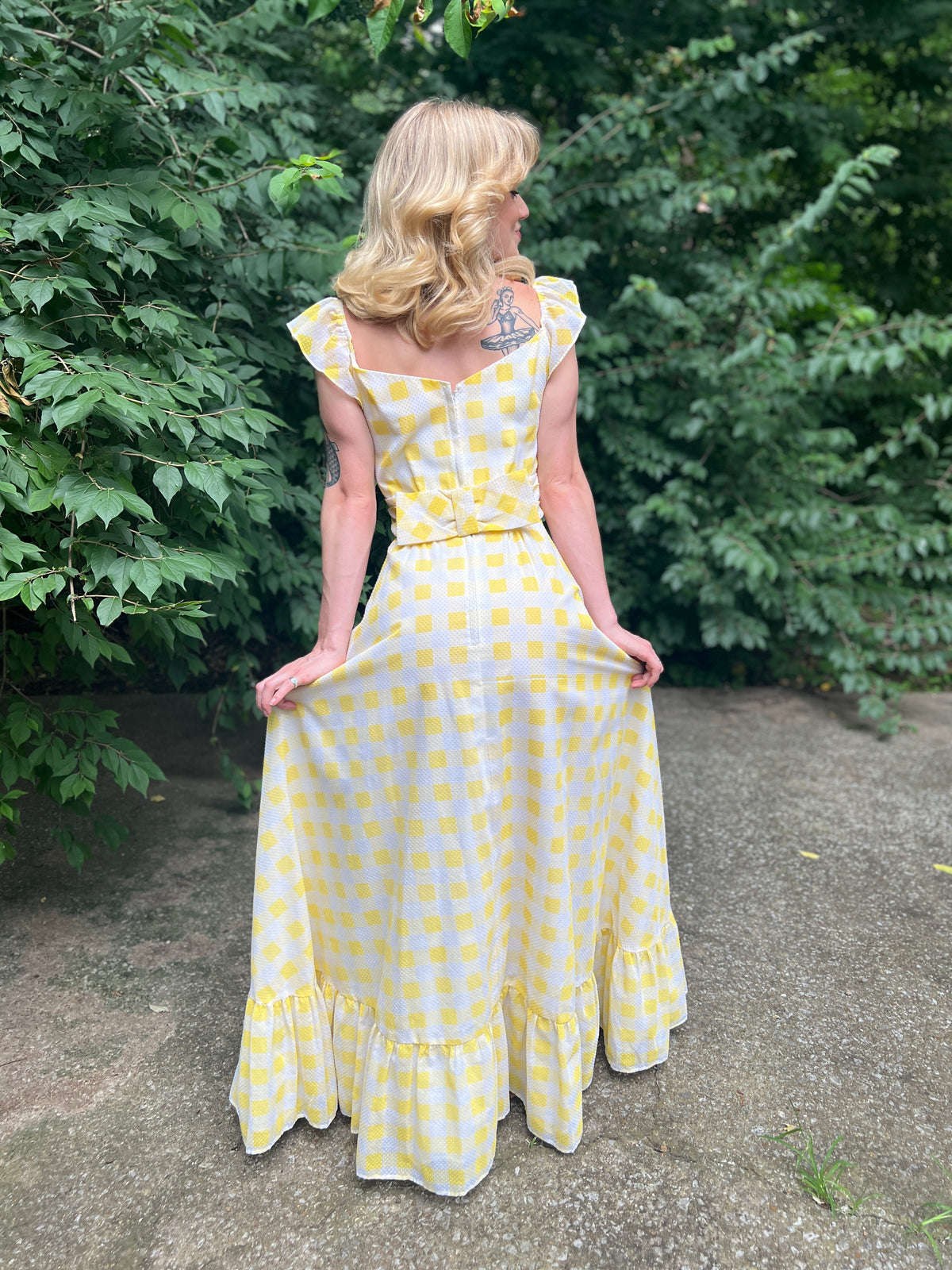 Back view on the model holding the skirt out, showing the waist bow, zipper and ruffled hem