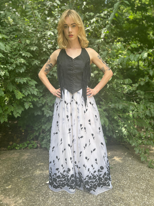 White maxi skirt with a sheer overlay and black velvet floral flocking, worn by a model with a fringe vest