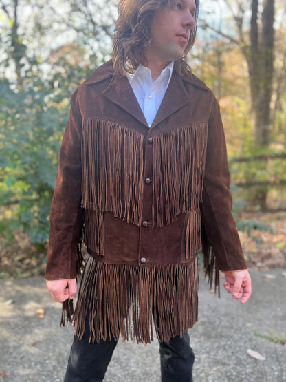 Dark brown suede coat with long fringe on the shoulders, pockets and hem and four front buttons, worn by a model