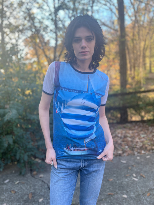 Blue knit short-sleeve shirt with a photo print of a sailboat on the front, worn by a model