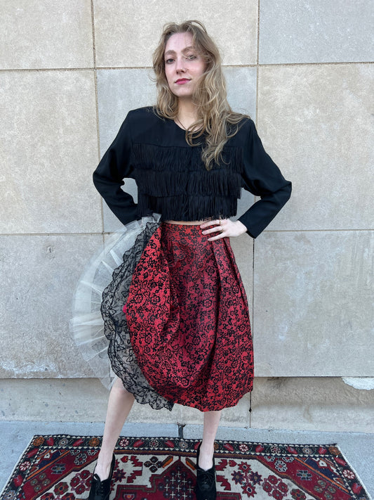 Red taffeta skirt with black floral flocking and pleats at the waist, worn by a model with a fringe jacket