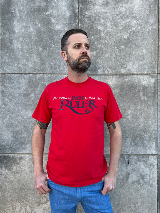 Red short sleeve t-shirt with text reading Give a man an inch, he thinks he's a ruler, worn by a model