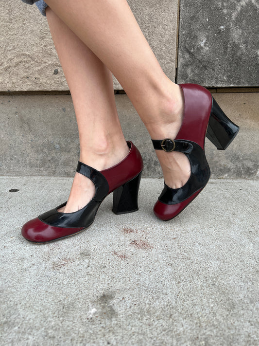 Pair of red and black patent leather Mary Jane shoes with thick straps and chunky heels, worn by a model