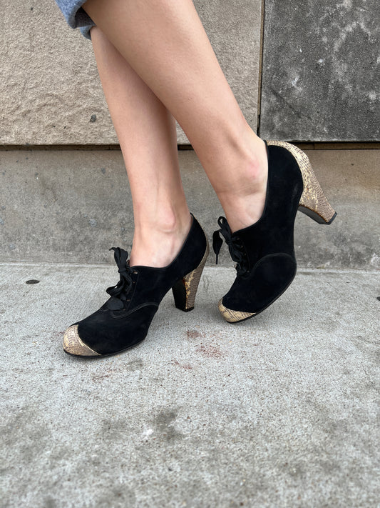 Pair of black suede lace-up shoes with reptile toe caps and heels, worn by a model, side view