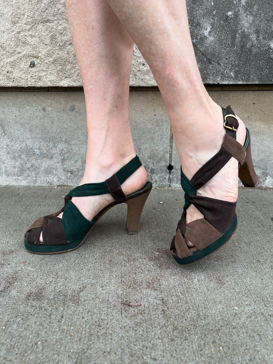 Pair of green and brown suede platform shoes with twisted straps across the top and a side buckle, worn by a model