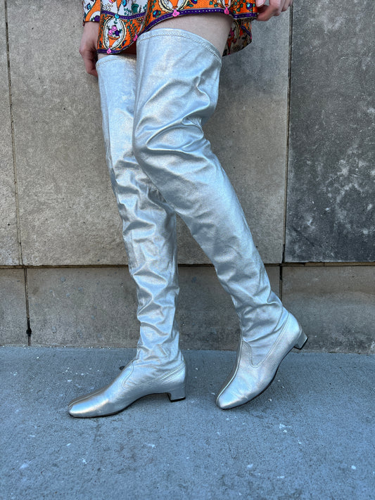 Pair of silver lurex thigh high boots with low heels, worn by a model with a mini dress