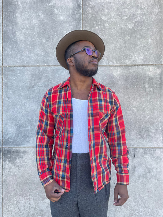 Red, tan, blue and black plaid flannel shirt worn open over a tank top by a model