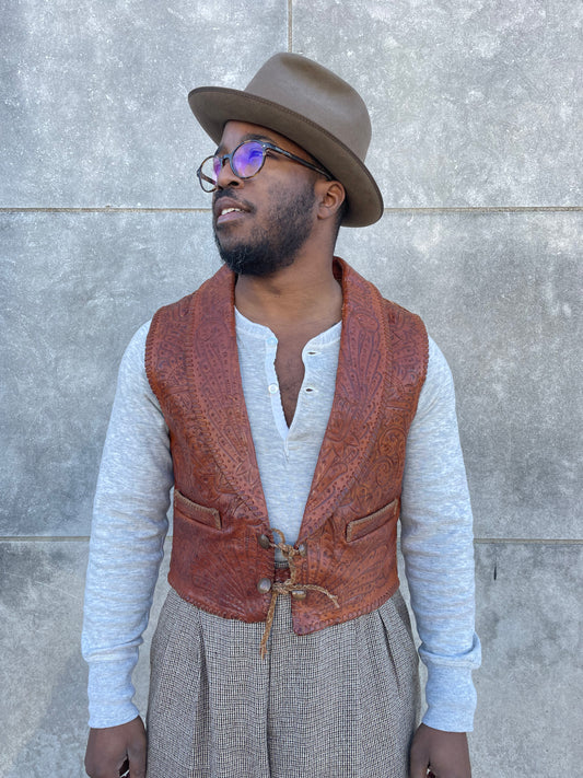 Brown tooled leather vest with pockets and braided leather tie closure, worn by a model