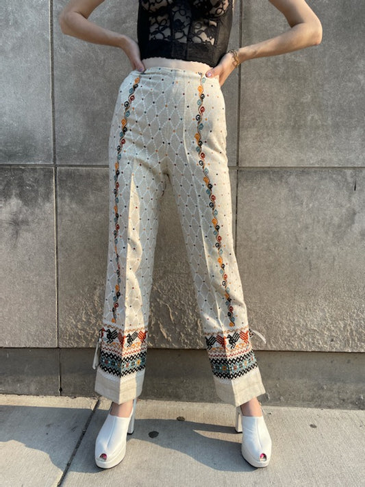 Tan and white diamond pattern pants with patterned borders at the hems, worn by a model, front view