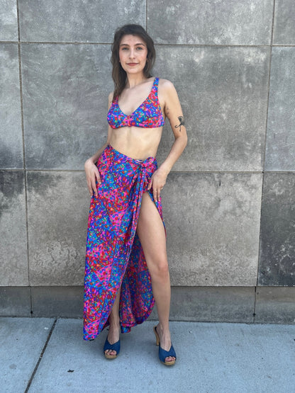 Pink, purple and green print bikini top and wrap skirt with a high slit, worn by a model