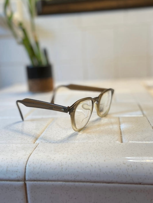 Angled view of the eyeglasses on a tile counter showing an arm and the frame shape