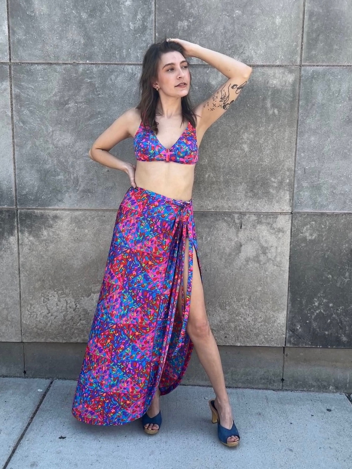 Bikini top and wrap skirt on the model with one arm raised, showing the slit