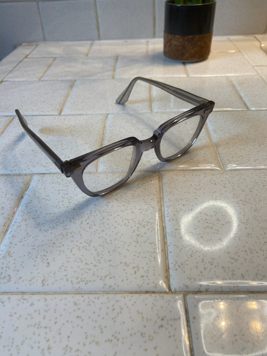 Grey translucent eyeglasses sitting angled on a tile counter, showing the frame front with both arms open