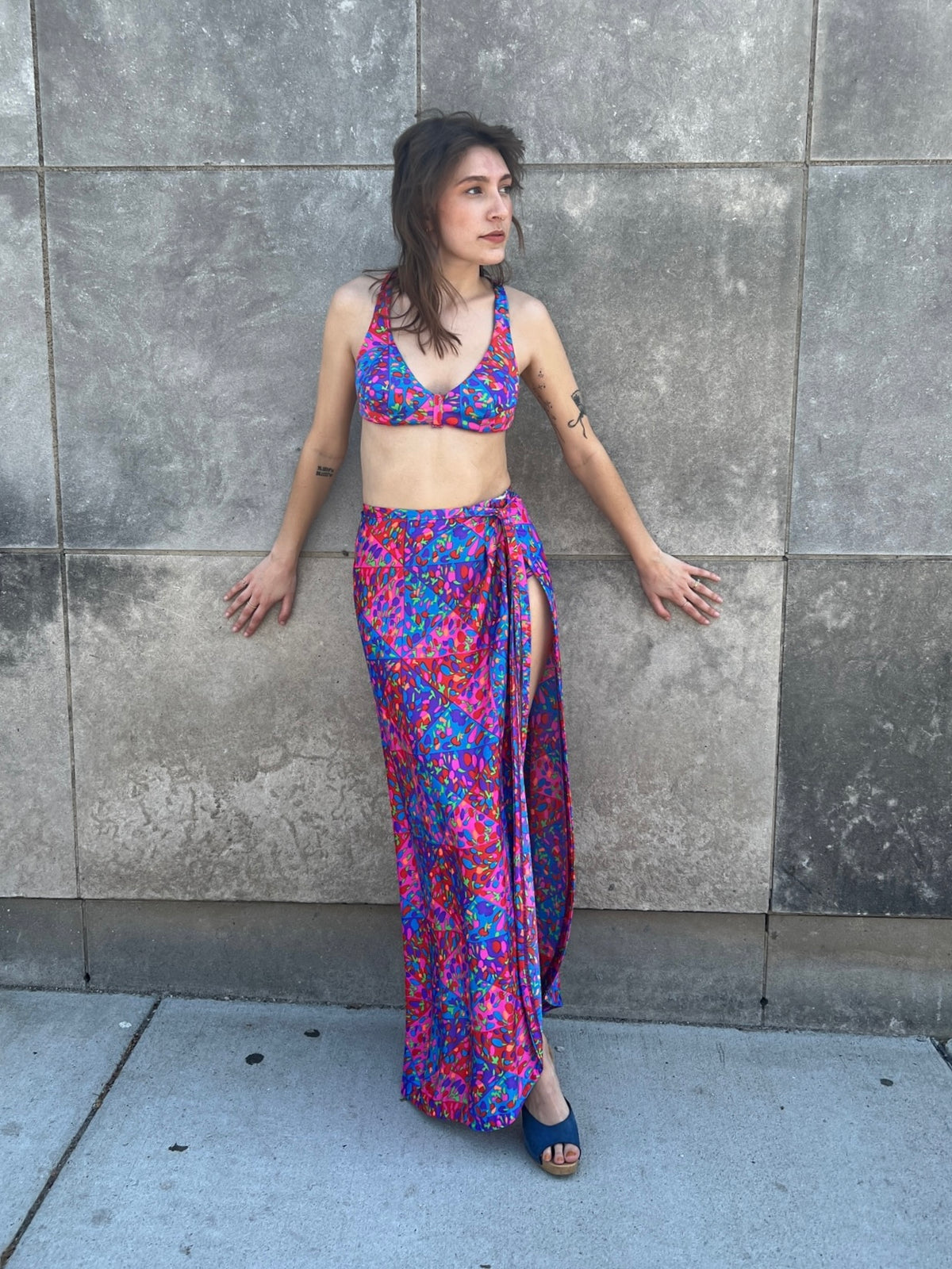 Bikini top and wrap skirt on the model leaning on a wall, showing the slit