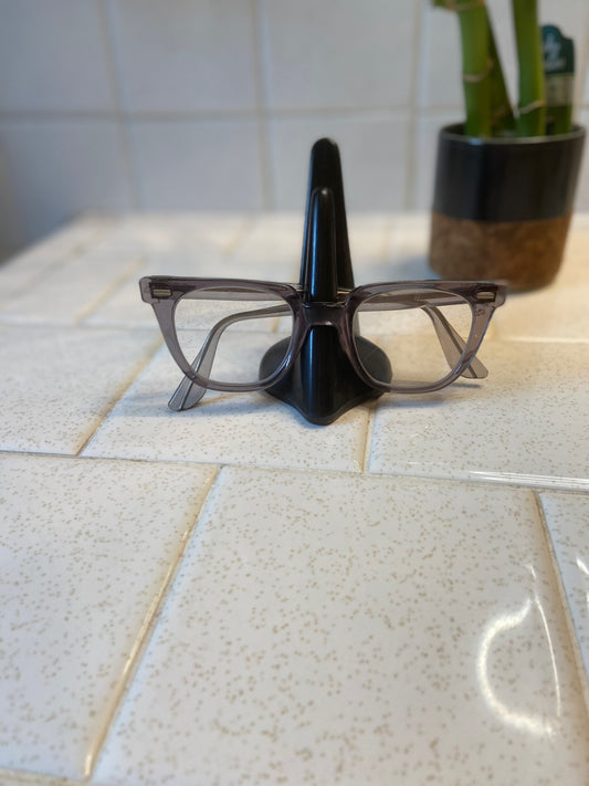 Grey translucent square frame eyeglasses on a nose-shaped holder on a tile counter